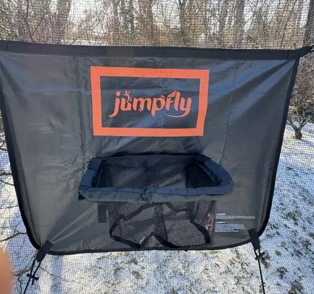 Jumpfly basketball hoop for trampoline with storage net in a snowy yard.